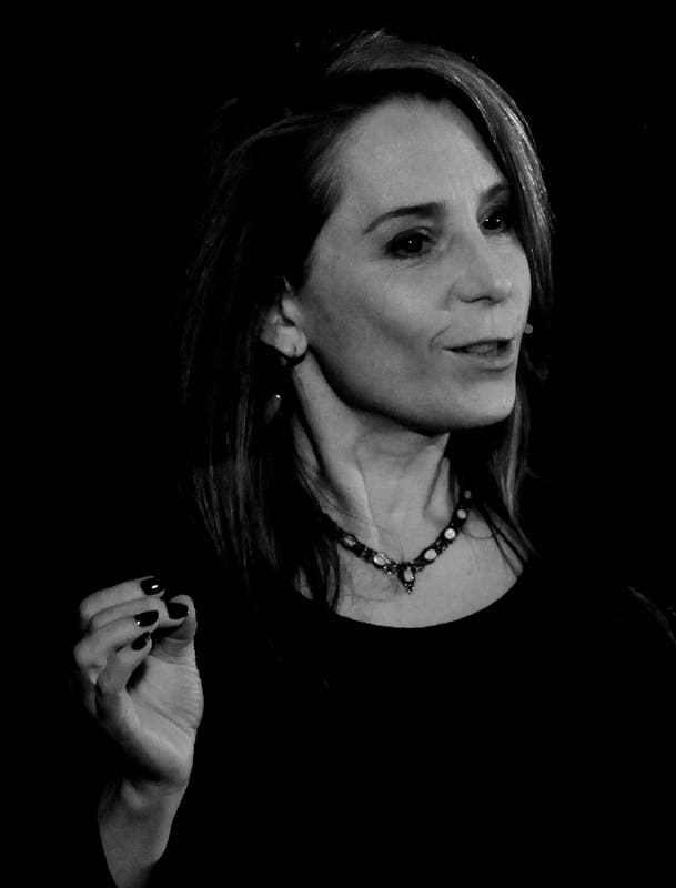 A woman with long hair and a necklace. The image is dark and monochrome. This is Deborah Hyde.