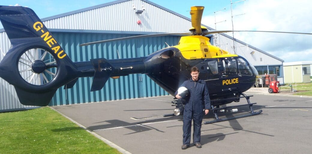 Dr Laurance Donnelly stands in front of a police helicopter outside an aircraft hangar.