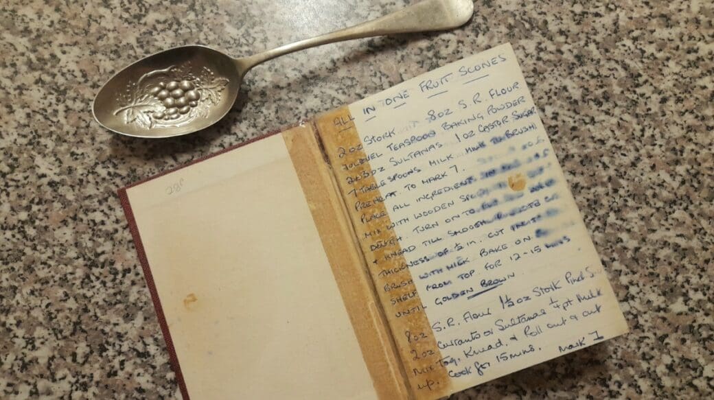 A recipe for all-in-one fruit scones. It's written on the first page of an old lined-notebook, which has been taped back together on the spine. The page is marked, and there are stains across the instructions. The recipe is written in fading blue ink.