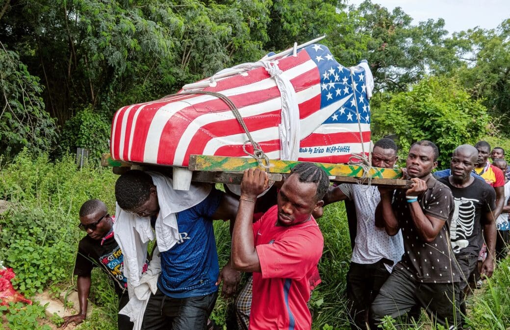 A group of pallbearers carry a trainer-shaped fantasy coffin painted in red, white and blue.