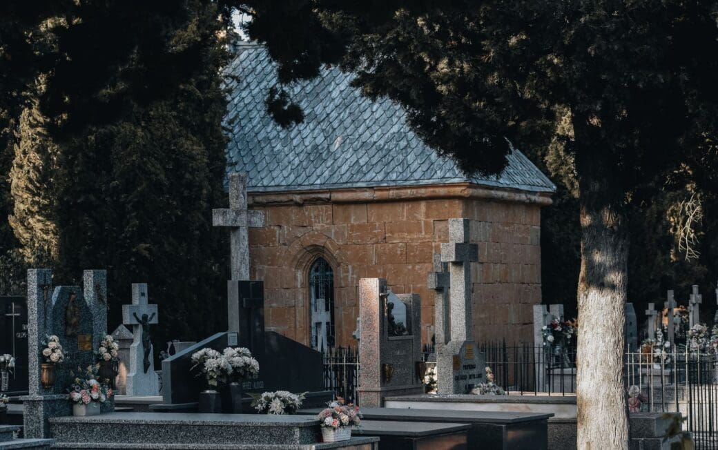 Peaceful cemetery with tombstones and a charming red-stone chapel surrounded by trees.